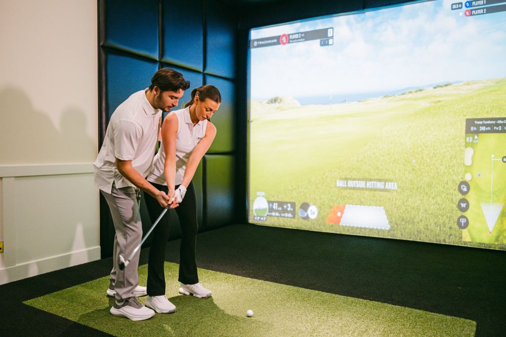 A woman being coached in a golf simulator