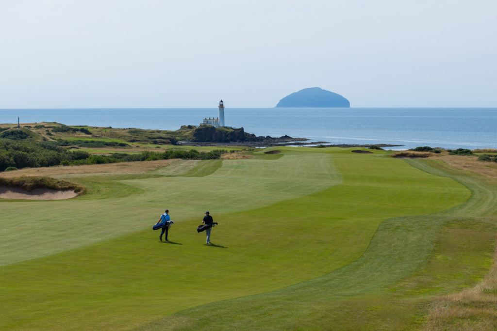 Two golfers walking a links fairway toward the lighthouse