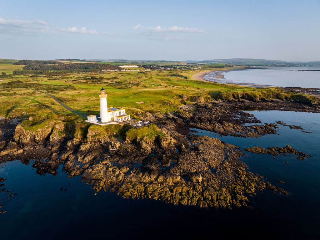 Aerial view of a lighthouse on a rocky coast beside the links
